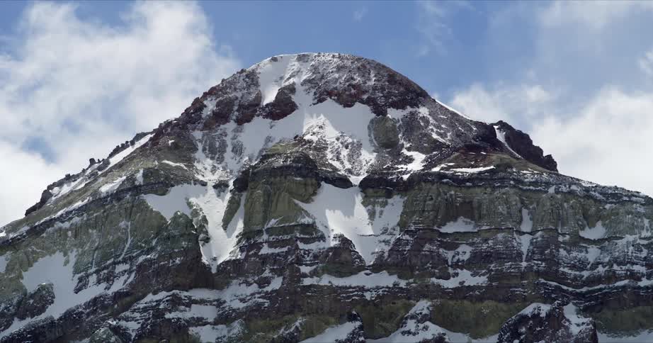 Clouds flow over a rounded snowy mountain timelapse