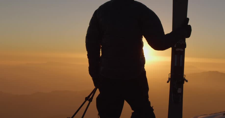 A man holding skis looks to the sunset