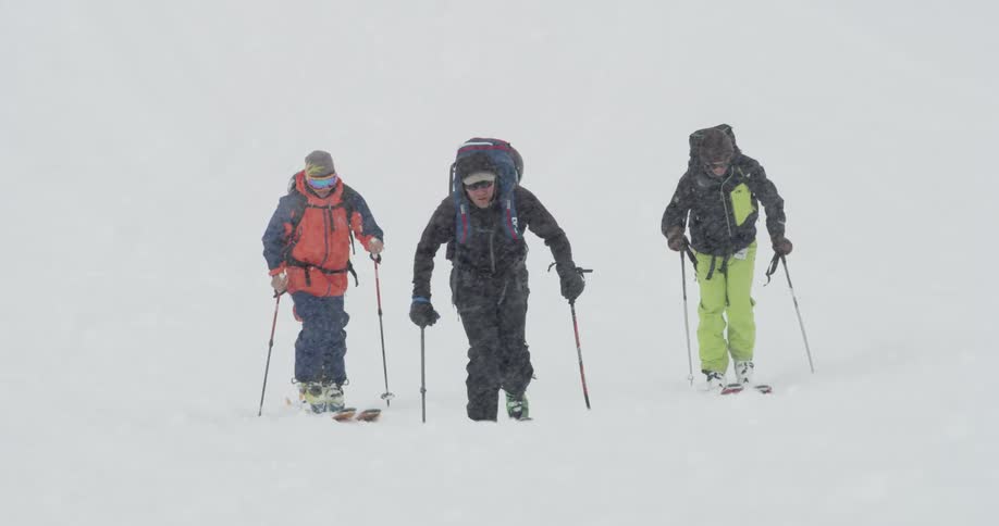 Three men ski through a snowstorm