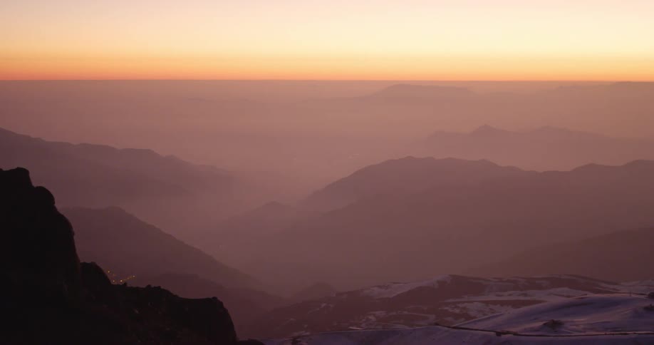 A snowy mountain range at sunset pan