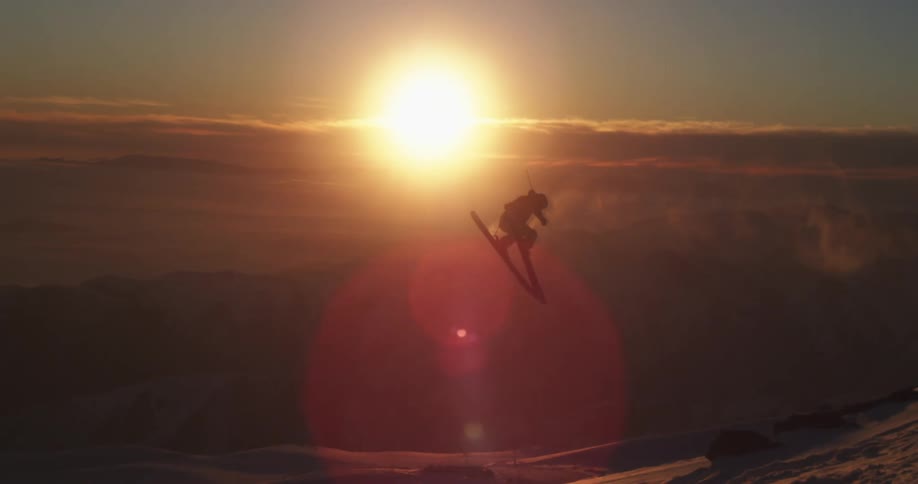 A skier jumps and spins through a sunset