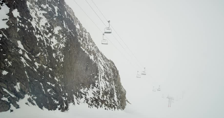 Ski lifts hang motionless over a mountain as snow falls from a cloudy sky