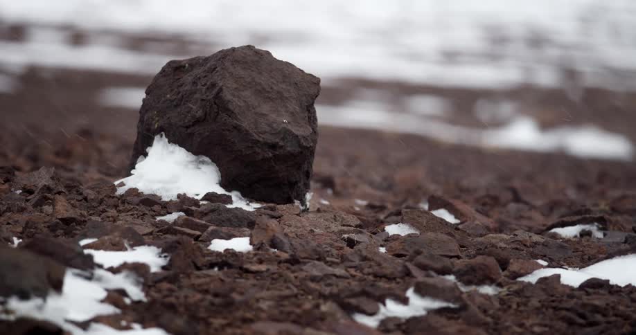 Snow falls on ice dotted rocky ground