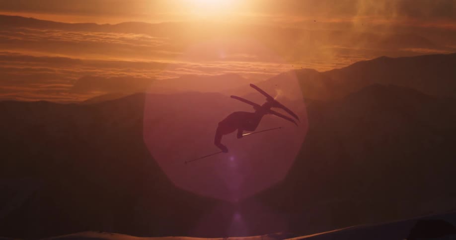 A skier does a back flip off a jump in snowy mountains at sunset