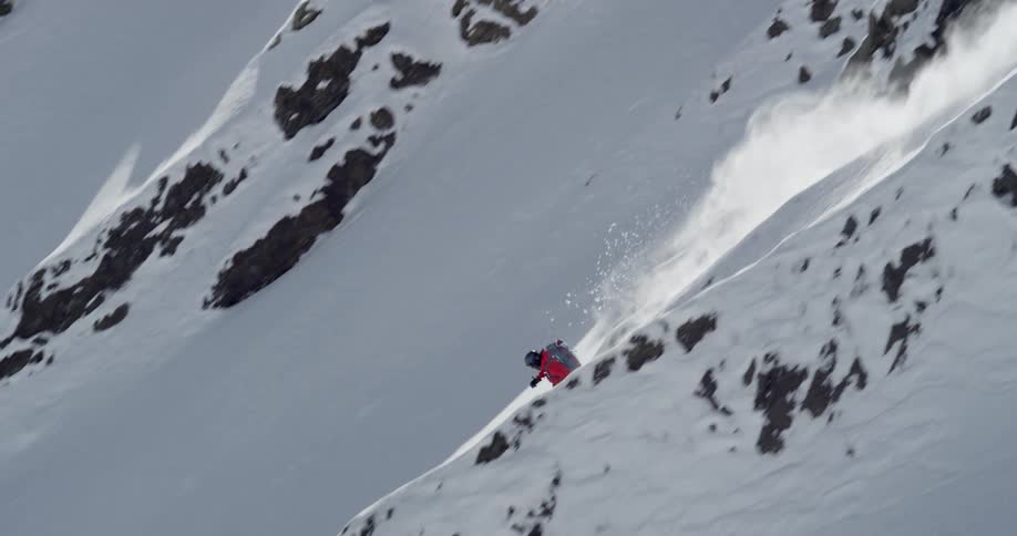 Skier wearing backpack skis down steep slope