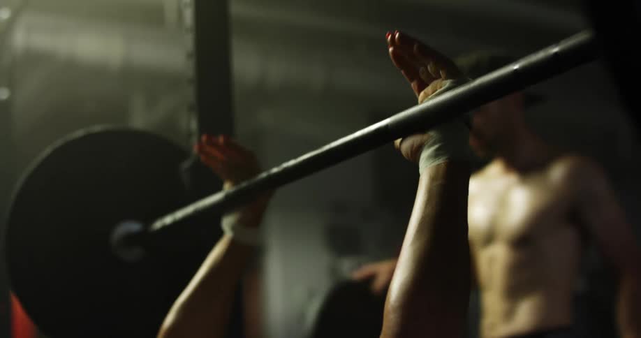 A man walks over to watch another man bench press weights