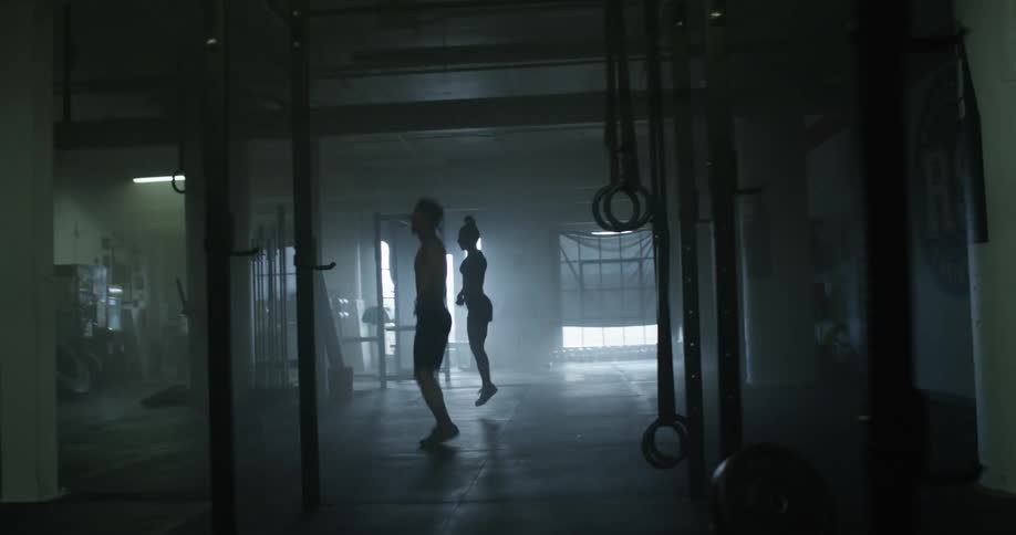 A man and woman jump rope side by side in a dimly lit gym