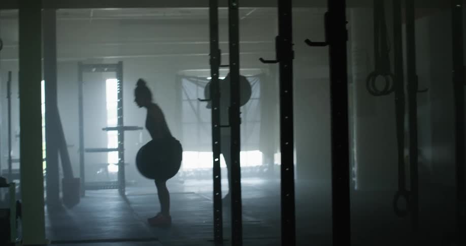 Two women lift large weight bars in dimly lit gym