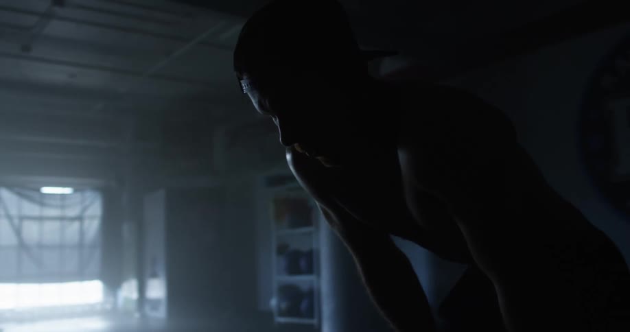 Muscular man with a cap taking a break after workout is silhouetted in gym