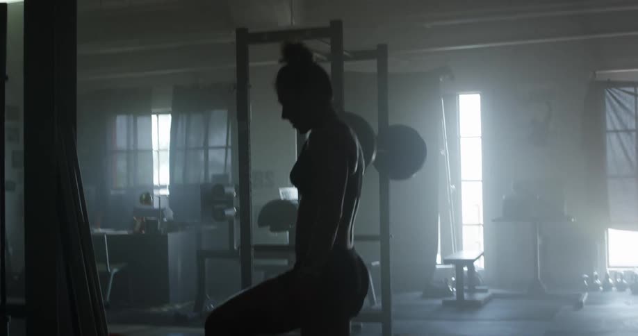 A woman in athletic wear stands in a dimly lit gym filled with exercising equipment