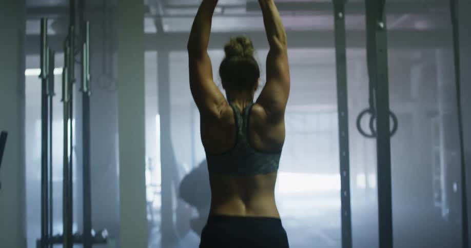 Sweaty muscular woman with sports bra warms up for workout in a gym