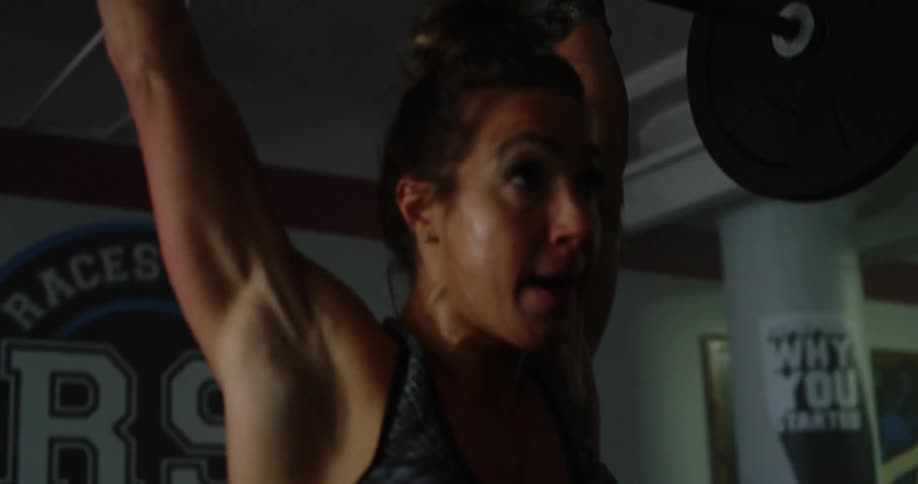 A muscular young woman lifts heavy weights up off the floor and lifts them over her head