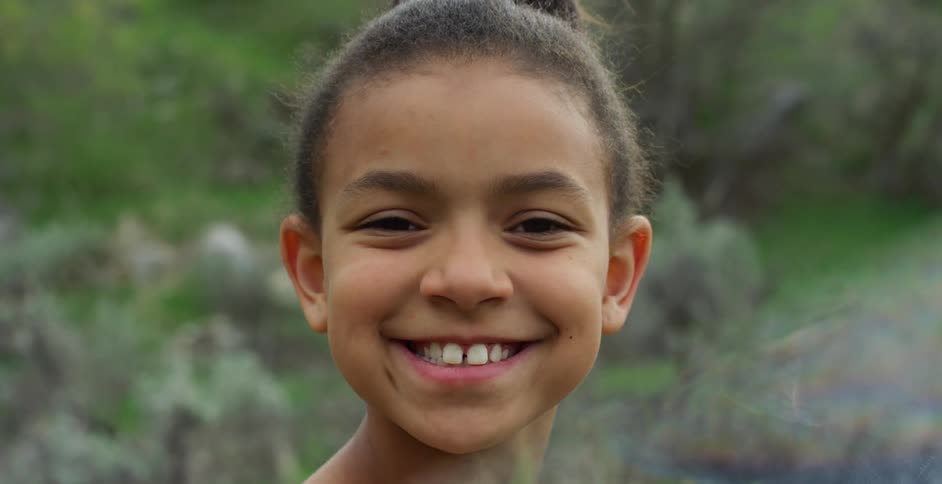 Close up of a girlss face smiling at the camera in a garden