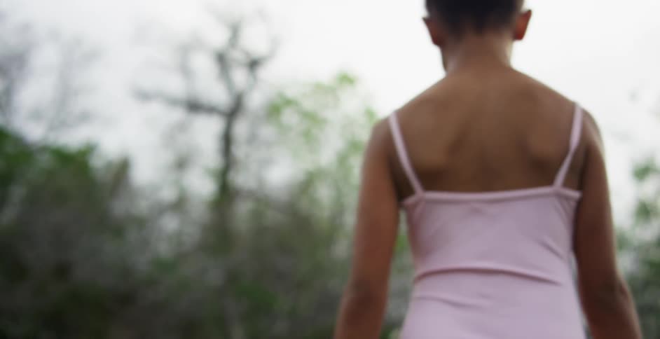 A young girl wearing a pink ballerinas leotard walks alone through the forest