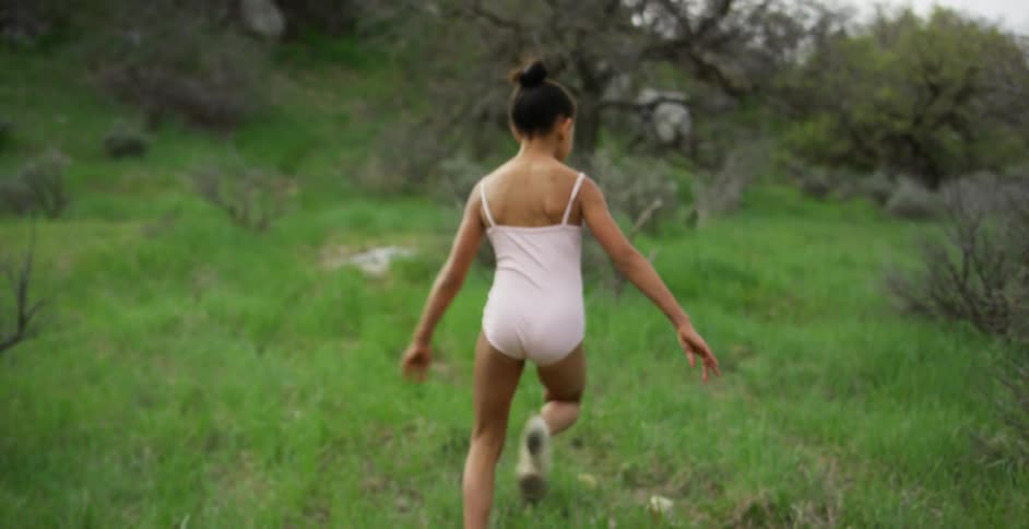 A young girl in a bathing suit running across the grass towards the water