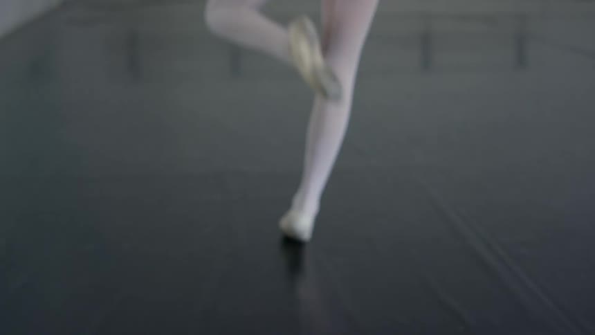 A young ballerina performs ballet moves on a mat in a ballet studio