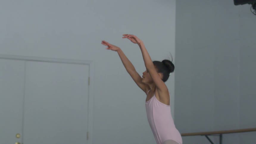 Young dancer in pink leotard and tights stretches in dance studio near dance bar