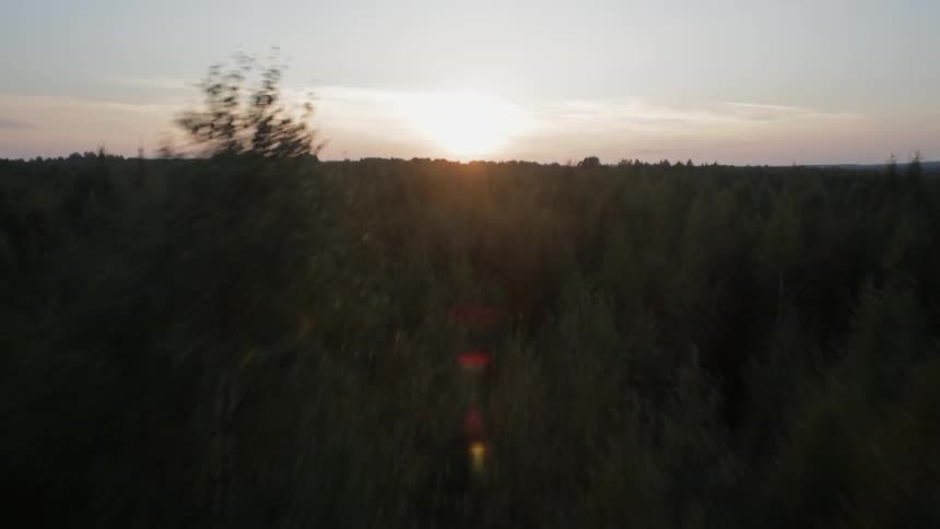 Moving fast over a forest with barns over a field and the sun setting