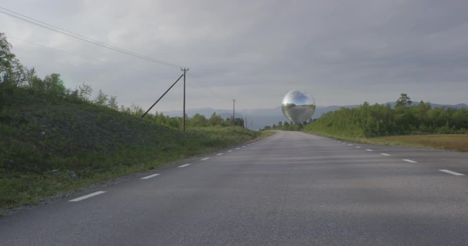 A silver ball hovers over a country road