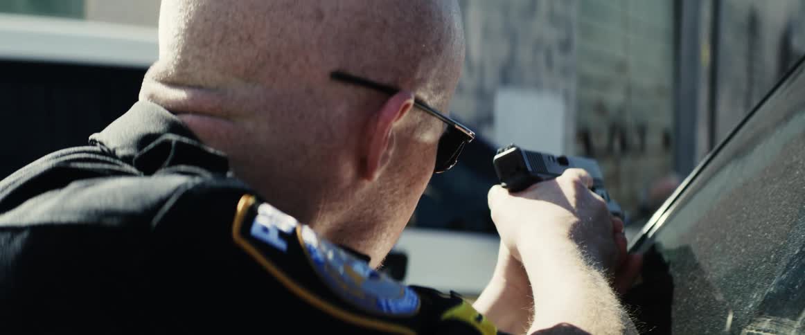 Law enforcement personnel shelter behind vehicles aiming weapons toward rundown building