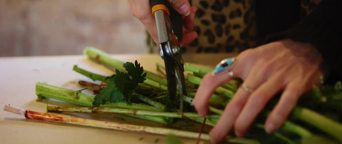 A woman uses a set of pruning shears to cut the steam of a bouquet of flowers