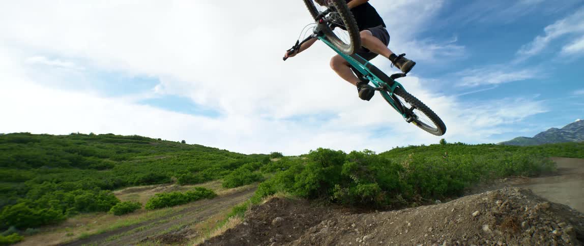 A man with a bike and helmet jumping over a pile of dirt with grass in the background