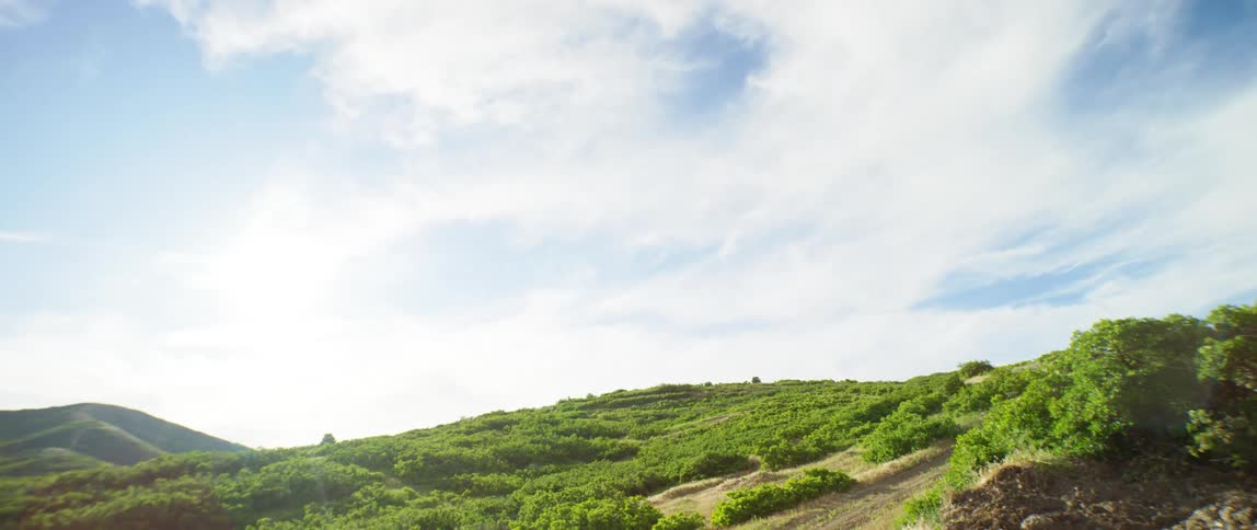 Two people ride mountain bikes and jump rock piles in a rural area