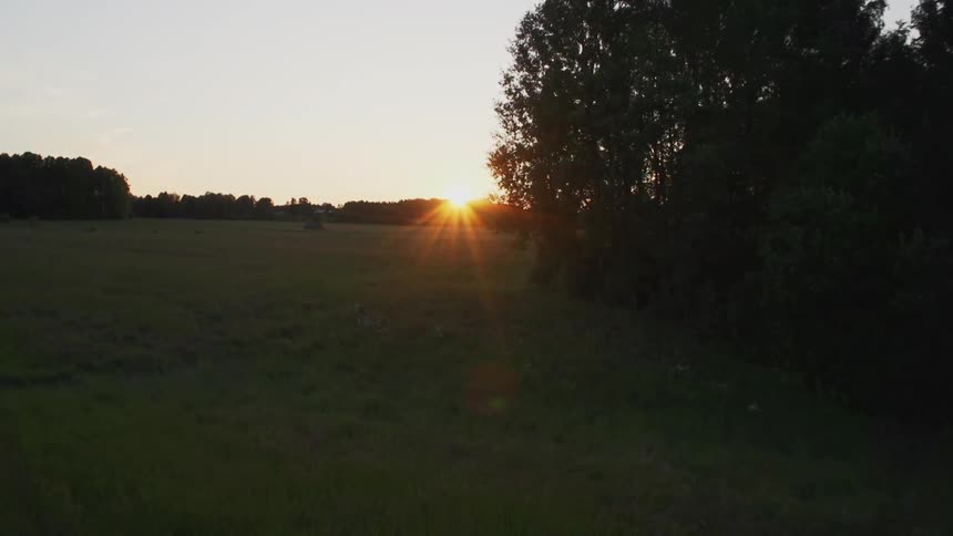 An abandoned barn in a field with trees at sunset