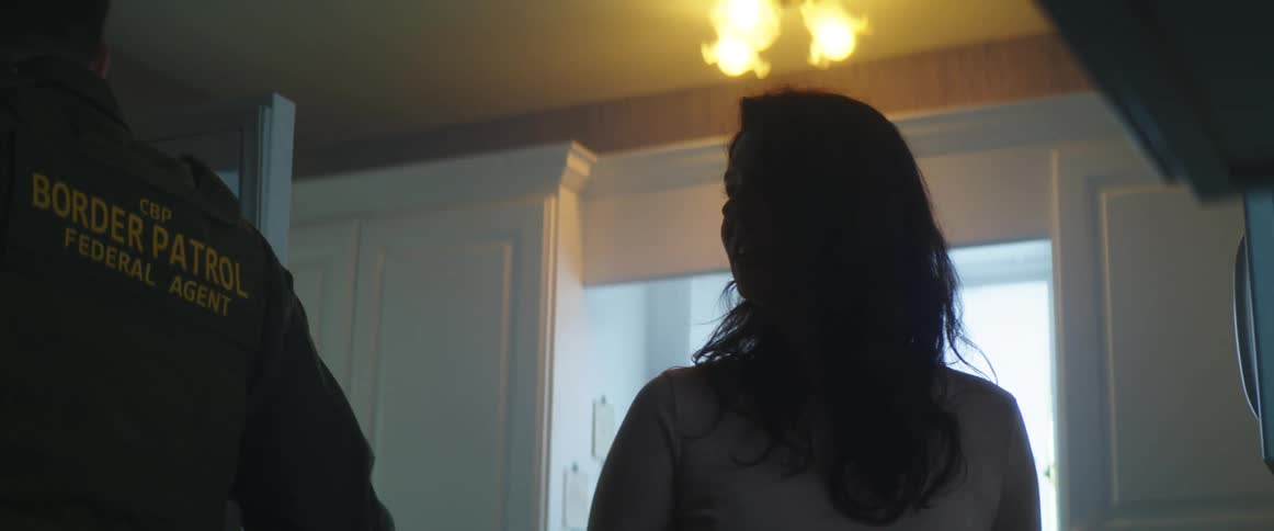A border patrol agent in a kitchen with a woman talking to each other