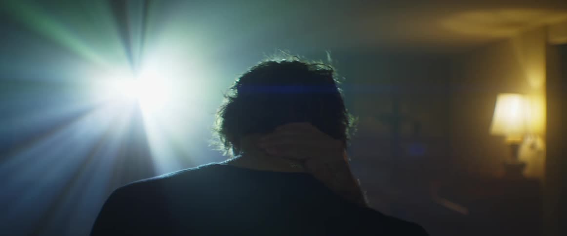 Man standing in front of bright flickering light from projector massages neck