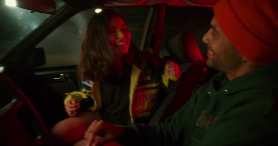 A teenage girl and boy laugh and dance and sing in the front seat of a car