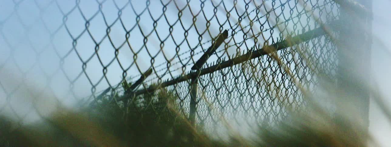 A chain link fence with barbed wire across the top under a clear daytime sky
