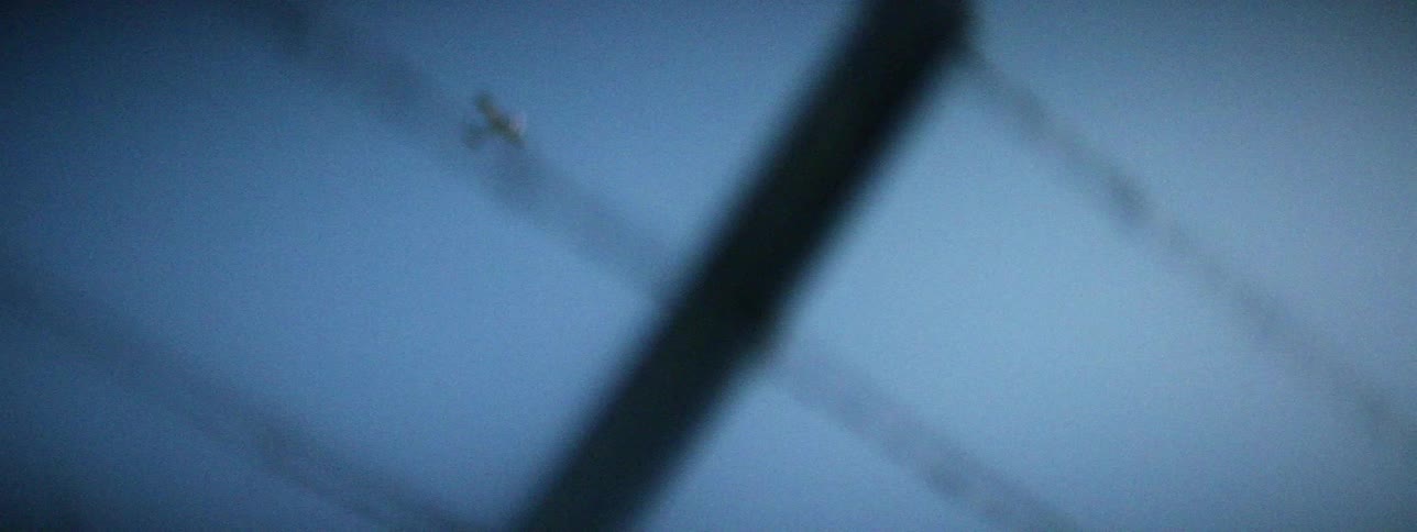 Personal plane flies through clear blue sky over barbed wire topped chain link fence