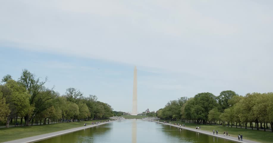 People walking in a public park beside a river with a large monument at the end