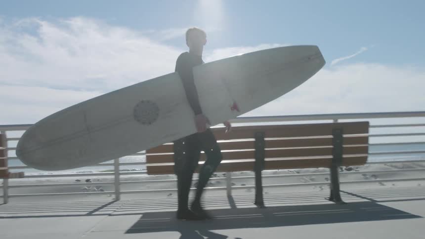 A man is walking along the boardwalk carrying a surfboard