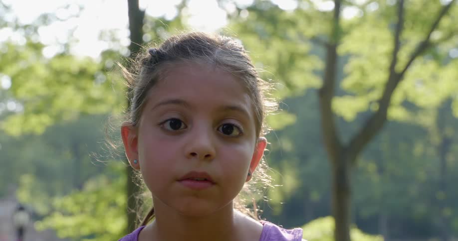 Child with a ponytail and dark brown eyes faces the camera with eye contact