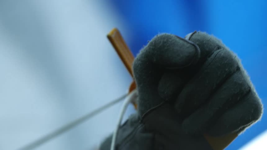 Man wearing gray gloves stretches thin rope attached to wood