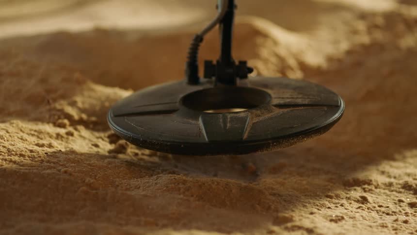 Disk of a metal detector scanning over the yellow sands
