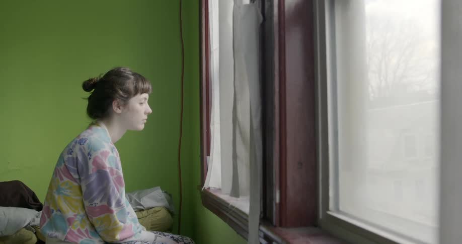 A woman looks out the window in a green room