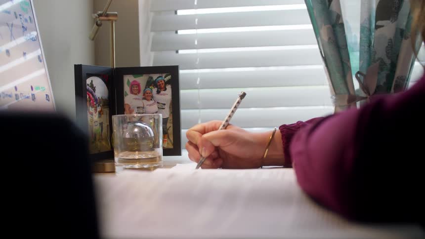Woman with a purple sweater sits at a desk and writes down with a pen