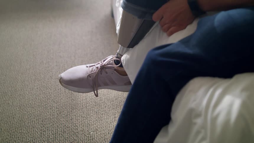 Woman lift the boot of her jeans over her prosthetic legs sitting in bed at home
