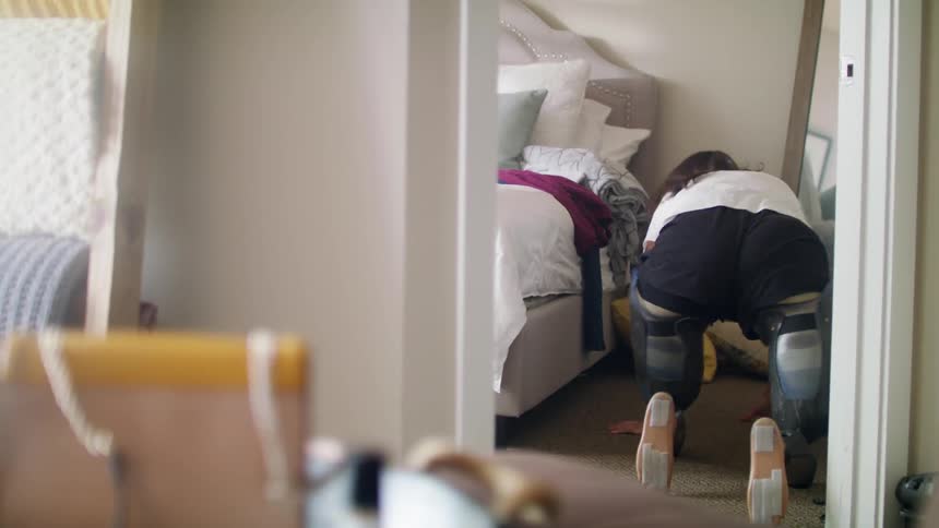 A female amputee rolls over on the floor and then kneels beside her bed