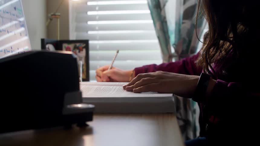 A woman sits at a desk writing in a book