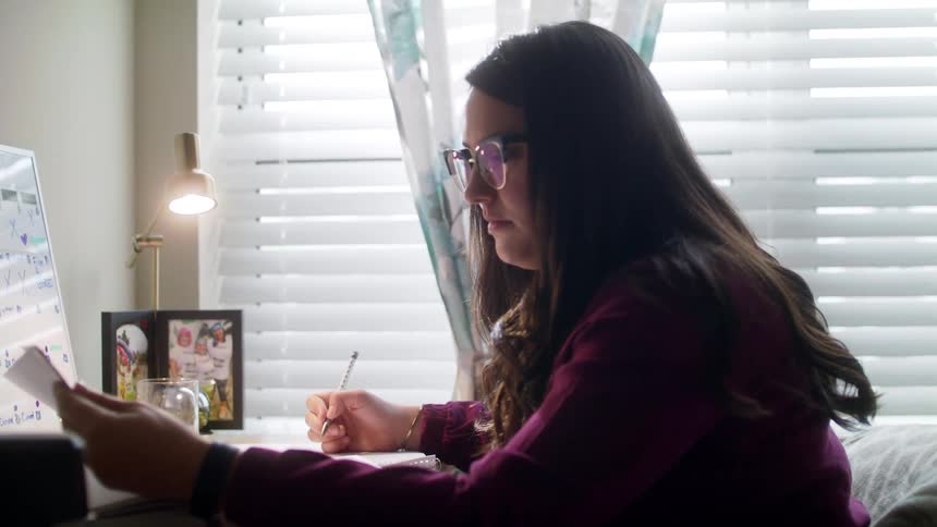 A young woman studies with a pen in her right hand as she flips pages in a large textbook