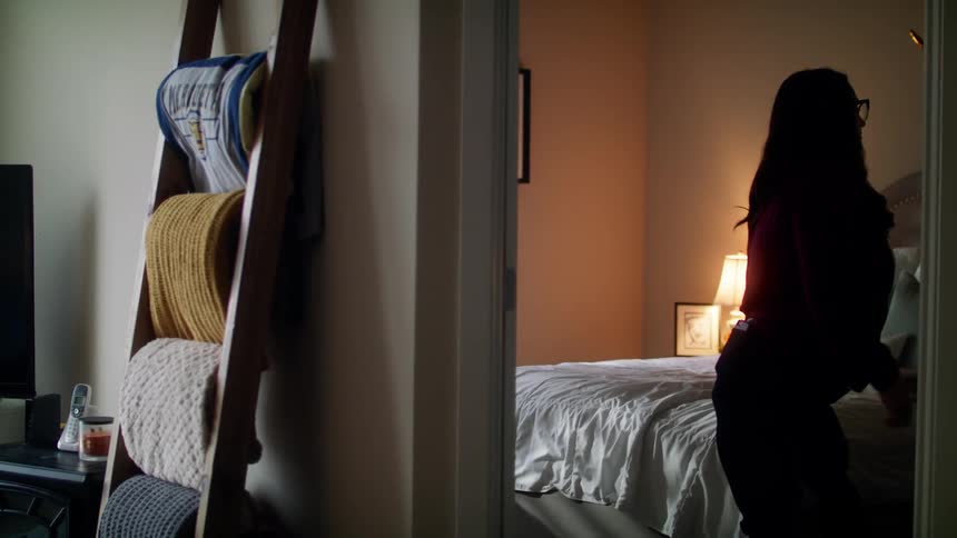 Pregnant woman with a white t shirt and glasses walking in bedroom is silhouetted