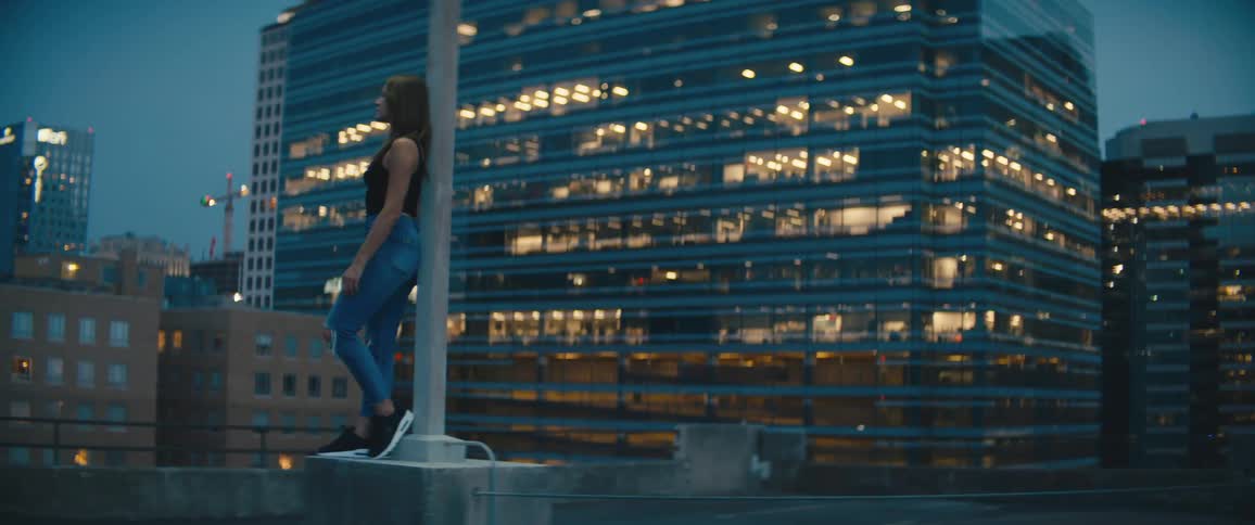 Woman leans against pole looking out at downtown city skyscrapers