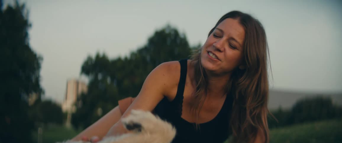 Woman lays in the grass on a park petting her dog at sunset