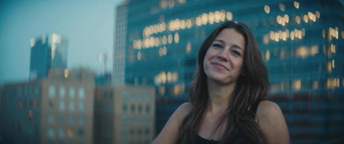 A woman smiles as she stands in front of a city skyline