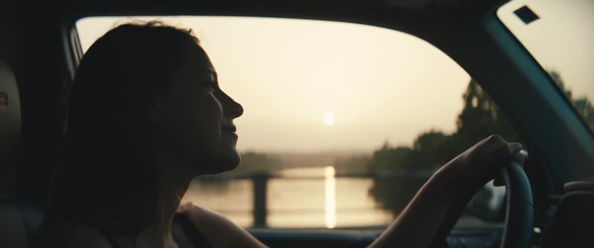 A woman drives her car past a lake and other cars on the road