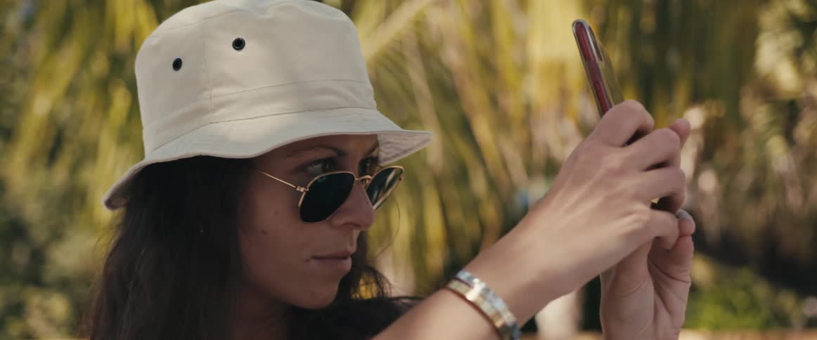 Brunette woman with a white hat and glasses takes a selfie during holiday